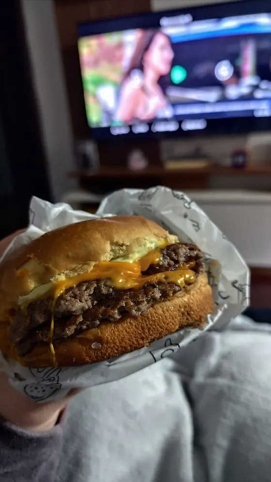 Hambúrguer de delivery na mão, em frente à TV, no fim do dia